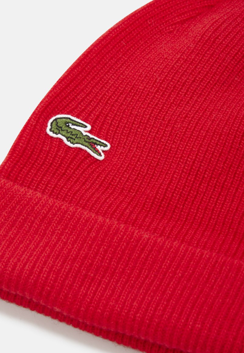 Beanie rosso lavorato a maglia con un motivo testurizzato e un logo di coccodrillo verde ricamato sul lato.