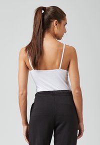 Witte top met dunne bandjes en een eenvoudig ontwerp, gecombineerd met zwarte joggers met elastische taille. De outfit heeft een relaxte pasvorm en minimale details.