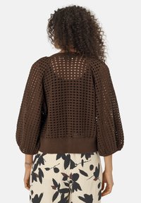 Pull en tricot marron avec un motif de tissage lâche et ouvert, des manches bouffantes et un ourlet ajusté. Le dos présente un design similaire ouvert.