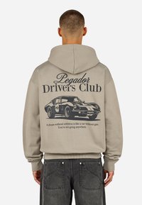 Felpa beige con cappuccio regolabile, caratterizzata da una grafica nera di un'auto d'epoca e la scritta "Pegador Driver's Club" sulla schiena.