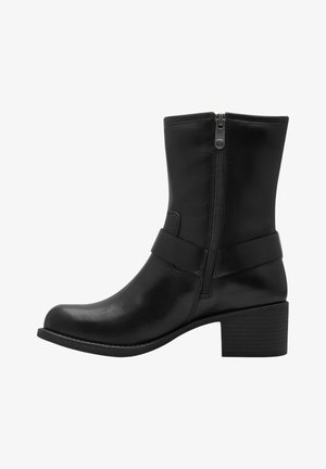 Bottine noire en cuir avec tige droite, fermeture éclair sur le côté et un large détail de sangle. Talon épais avec une base texturée. Fini lisse.