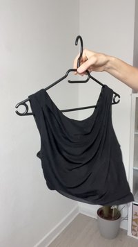 Top negru, fără mâneci, dintr-un material moale, cu un design fluid și un decolteu rotund, expus pe un umeraș negru.