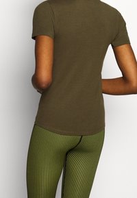 Camiseta de color verde oliva con mangas cortas y escote redondo, combinada con leggings verdes rayados verticalmente. Tela de algodón suave.