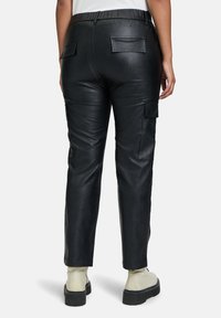 Zwarte neplederen cargobroek met een elastische tailleband, twee achterzakken en een ontspannen pasvorm, die eindigt bij de enkels.