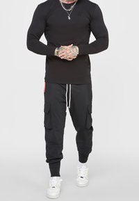 Černé tričko s dlouhým rukávem a kulatým výstřihem, v kombinaci s černými cargo tepláky s bočními kapsami a bílou šňůrkou, doplněné bílými teniskami.