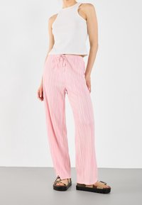 Jasnoróżowe spodnie o szerokich nogawkach z pionowymi białymi paskami, z elastycznym paskiem w talii i sznurkiem do regulacji. Zestawione z białą bluzką bez rękawów.