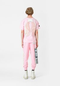 Conjunto de algodón rosa que incluye una camiseta con gráficos de alas de ángel y pantalones de chándal a juego, adornados con acentos laterales y un detalle de etiqueta.