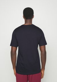 Granatowy, bawełniany t-shirt z krótkimi rękawami i okrągłym dekoltem, pokazany od tyłu. Gładka faktura, prosty wzór, bez nadruków ani akcentów.