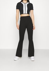 Mustat lyhyet kermit, joissa on etuvetoketju ja harmaat korostukset; yhdistetty mustiin leveneviin housuihin. Mallilla on päällään valkoiset lenkkarit.