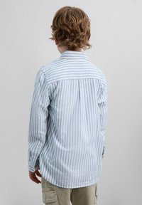 Camisa de botones a rayas en azul claro y blanco. Presenta un cuello, manga larga y un dobladillo curvado. La tela parece suave y ligera.