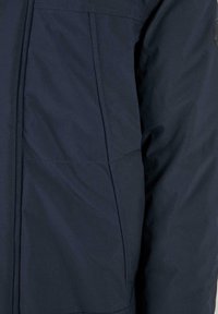 Giacca blu navy con una finitura liscia e opaca; presenta cuciture visibili e una tasca laterale; realizzata in materiale leggero e resistente all'acqua.