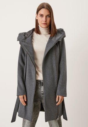 Gray wool blend coat with a hood, featuring a diagonal zip closure and side slits. Styled over a light turtleneck and jeans.