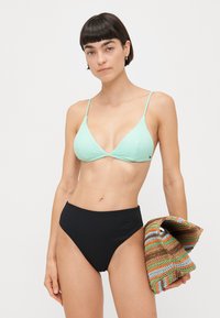 Bikini gornji dio u mint zelenoj boji s rebrastim uzorkom i tankim trakama, uz crne rebraste gaćice visokog struka, upotpunjene višenamjenskom torbom od tkanine u raznim bojama.