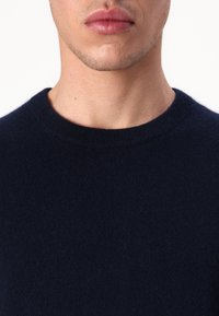 Pull en maille bleu marine à col rond, fabriqué dans un tissu doux ; vue rapprochée montrant la texture et les détails des coutures.