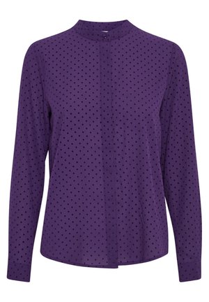Blouse violette à manches longues avec petits pois noirs, poignets boutonnés et fermeture par un bouton unique en haut du col montant.