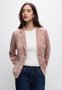Sametový sako v jemně růžov�é barvě, se střihaným designem, dvěma předními knoflíky a decentní texturou. V kombinaci s bílým topem a tmavými džínami.