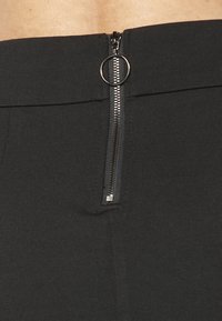Pantaloni neri attillati con una superficie liscia, una zip nascosta in vita con un pomello circolare e un design pulito e minimalista.