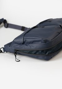 Donkerblauwe schoudertas van waterdicht materiaal, met twee ritscompartimenten, een verstelbare schouderband en kleine hardwareaccenten.