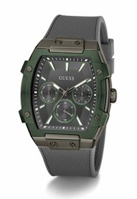 Montre rectangulaire verte avec un cadran noir texturé, trois sous-cadrans chronographiques, index horaires lumineux et un bracelet en caoutchouc gris.