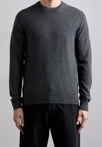 Grå stickad tröja med rundhals och långa ärmar, tillverkad i mjukt material, med normal passform och ribbade muddar och nederkant.