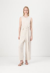 Combinaison en lin beige avec un devant à boutons, sans manches, taille cintrée et jambes larges avec revers aux chevilles.