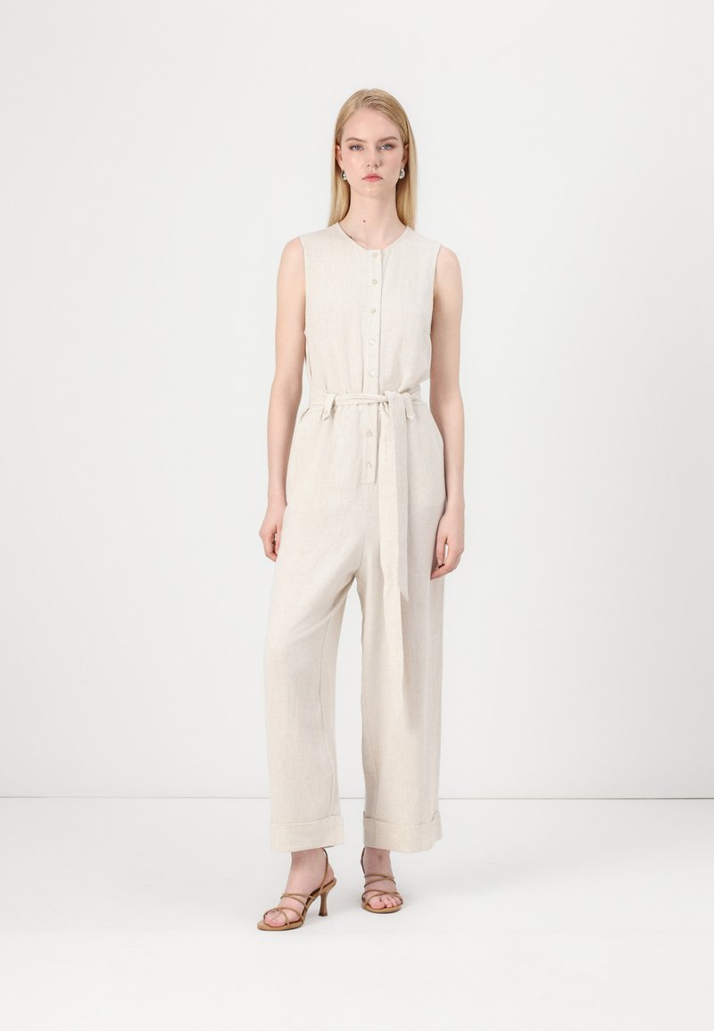Combinaison en lin beige avec un devant à boutons, sans manches, taille cintrée et jambes larges avec revers aux chevilles.