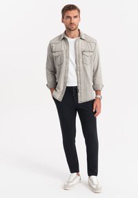 Lichtgrijze denim overhemd met borstzakken over een wit t-shirt, gecombineerd met zwarte joggingsbroek en lichtgrijze sneakers. Glad stof.