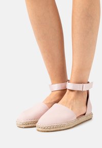 Lichtroze espadrilles met een canvas bovenkant, jute touwzool en enkelbandje. Kenmerkt zich door een ronde teen en open hiel ontwerp.