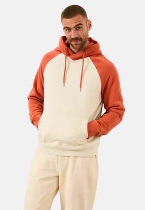 Kapuzenpullover mit cremefarbenem Körper, roten Raglanärmeln, frontaler Bauchtasche und verstellbaren Kordeln. Weiche Textur; minimalistisches Design.