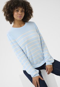 Pull bleu clair avec des rayures crème, encolure ronde et manches longues bouffantes ; texture douce et poignets côtelés ; associé à un jean en denim foncé.