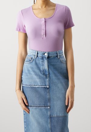 Femme portant un haut moulant à manches courtes côtelé lavande avec des boutons et une jupe en jean patchwork aux bords bruts.