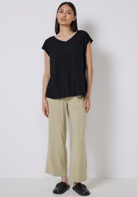 Sort, kortærmet, v-udskåret top parret med lysebeige, brede bukser. Modellen bærer sorte slip-on sko. Enkel design, afslappet look.