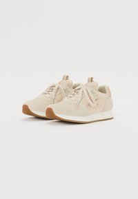 Jasnobeżowe sneakersy z mieszanką zamszu i materiału syntetycznego, sznurowadła oraz pomarańczowy akcent na pięcie. Gumowa podeszwa z bieżnikiem.