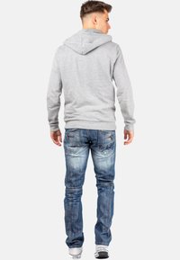 Sweatshirt à capuche gris avec une coupe décontractée, associé à un jean en denim bleu délavé avec des coutures décoratives et un branding subtil.
