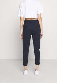 Marinblå tapered byxor med elastisk midja, två bakfickor och ett mjukt, slätt tyg. Matchas med vita sneakers.