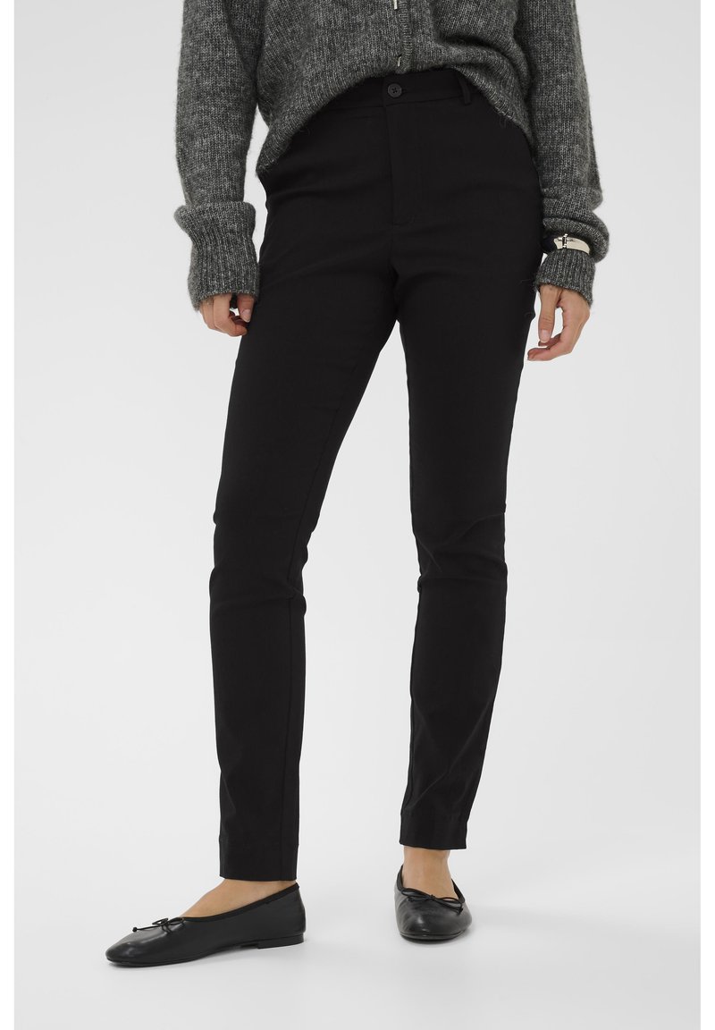 Mustad, slim-fit puuvillasegu kangast püksid, millel on kõrge vöökoht ja minimaalsed õmblusdetailid, koos mustade korteritega.