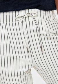 Witte gestreepte broek met een trekkoord in de taille. De strepen zijn zwart en de stof lijkt zacht met een gladde textuur.