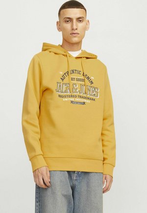 Gul hættejakke med en forgrundsgrafik i marineblå og hvid tekst, udstyret med en kængurulomme og ribbede manchetter. Bæres med lyseblå jeans.