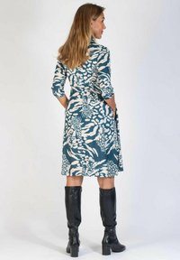 Blommönstrad klänning i teal och krämfärgat, med trekvartslånga ärmar, en åtsittande midja och en utsvängd kjol. Svarta knähöga stövlar kompletterar looken.