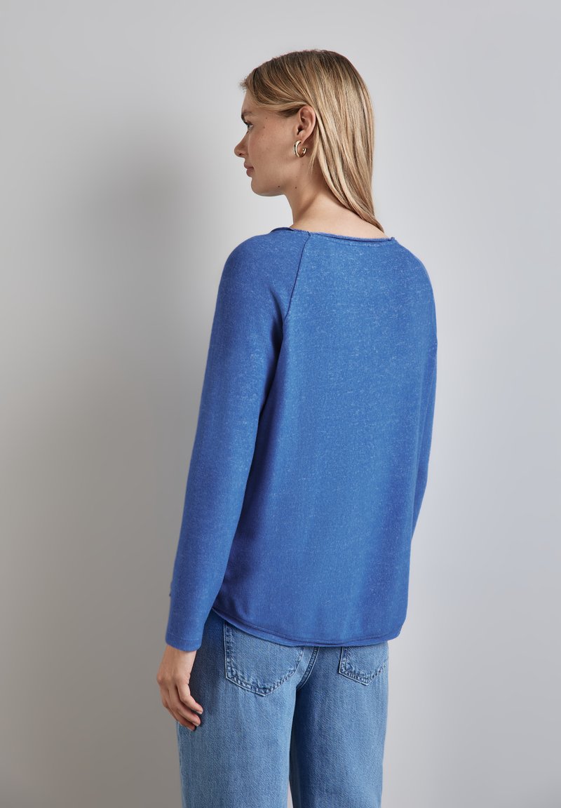Pull bleu avec une finition texturée, à manches longues et col rond, associé à un jean bleu clair, vu de dos.