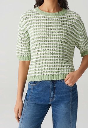 Pull en mailles vert clair avec des rayures blanches, manches courtes et tissu texturé ; associé à un jean en denim bleu.