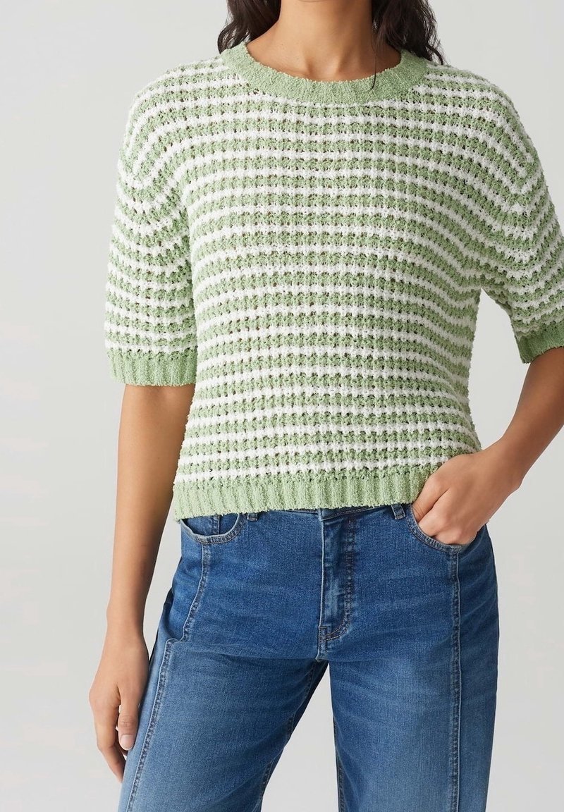 Maglione a maglia verde chiaro con strisce bianche, maniche corte e tessuto testurizzato; abbinato a jeans in denim blu.