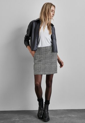 Svart och vit hundtandsskjorta tillsammans med en grå läderjacka och vit topp. Modellen bär svarta strumpbyxor och ankelboots.