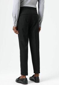 Zwarte op maat gemaakte broek met rechte pijpen, omgeslagen zomen en twee achterzakken, gecombineerd met een grijs shirt met lange mouwen en zwarte schoenen.