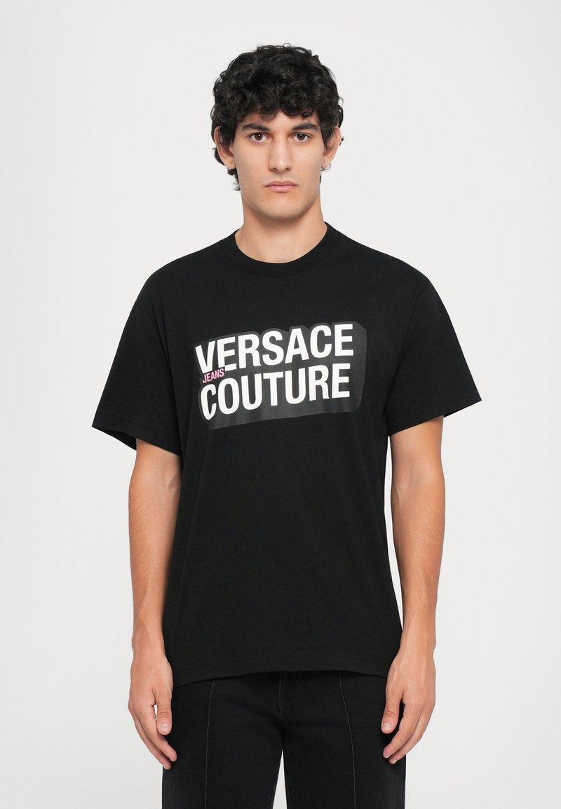 Melna kokvilnas T-krekls ar lielu balto un rozā "VERSACE JEANS COUTURE" logo priekšpusē. Īsas piedurknes, klasiskā apkakles dizains.