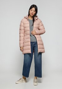 Jasnoróżowy, puszysty parka z kapturem, wyposażona w zamek błyskawiczny i boczne kieszenie; noszona na szarym topie, w połączeniu z szerokimi spodniami dżinsowymi i trampkami.