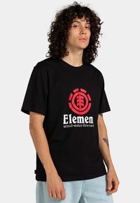 Camiseta negra de manga corta con un destacado logo rojo que presenta diseños de árbol y circulares. Confeccionada en material suave, de corte relajado y con acentos texturizados.
