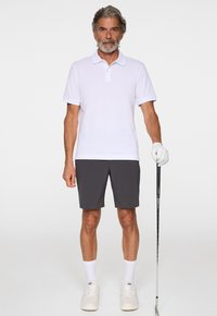 Vit pikétröja, grå shorts, vita sneakers och handskar. Står med golfklubba, avslappnad passform, korta ärmar, klassisk krage, enfaldig design.