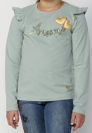 Dziecko ubrane w jasnozieloną koszulkę z długim rękawem z napisem "Awesome" z złotych cekinów oraz dwoma złotymi łatkami w kształcie serca, do tego niebieskie dżinsy z haftem motyla.