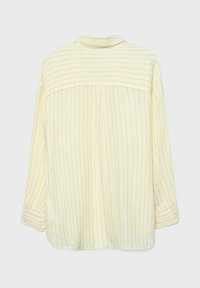 Kremasta majica z dolgimi rokavi s tankimi navpičnimi črnimi črtami in ramenskim delom s horizontalnimi črtami na hrbtu, manšete na gumbe.